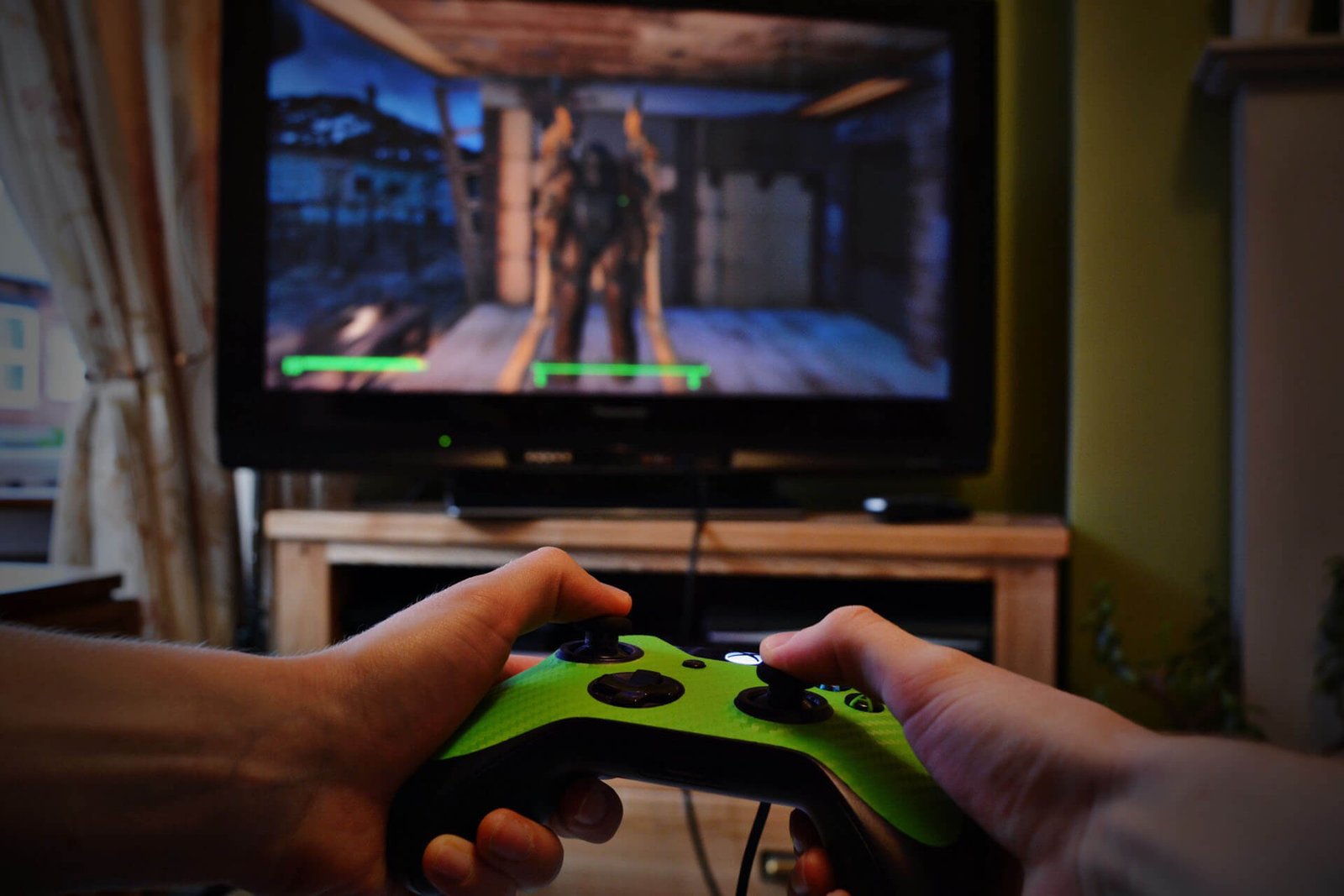 Person holding a bright green video game controller, focused on playing a game on a TV screen in a living room.