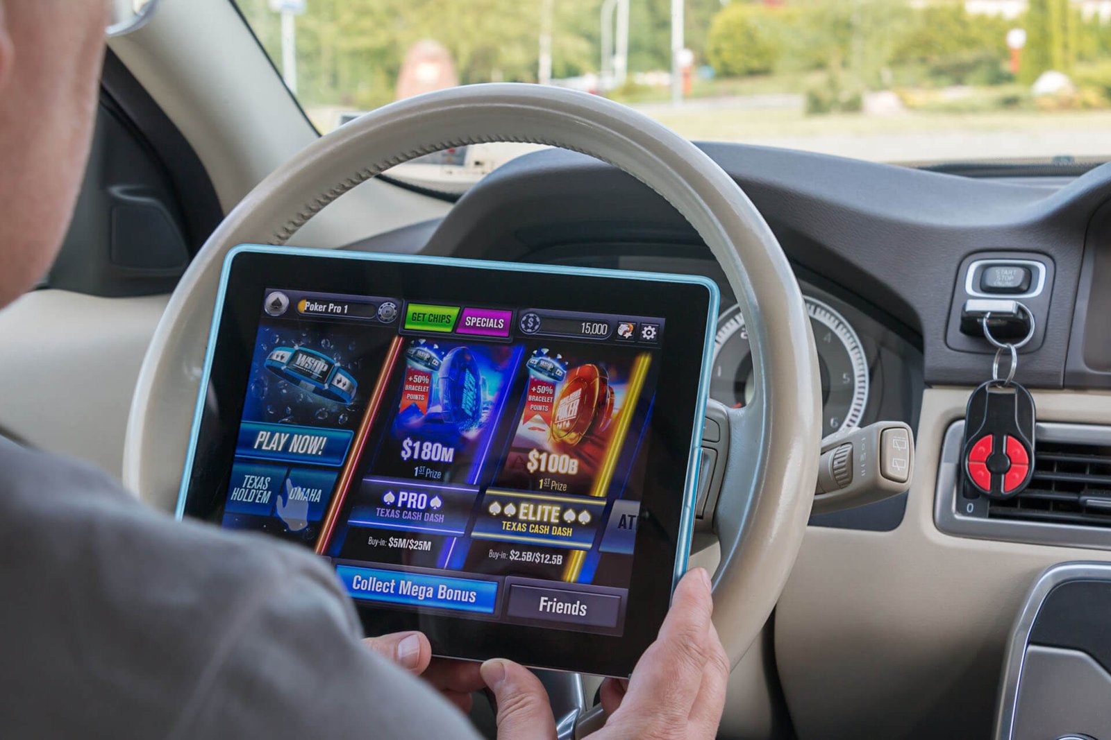Person in car holding a tablet displaying a colorful casino game interface on the screen, with steering wheel in view