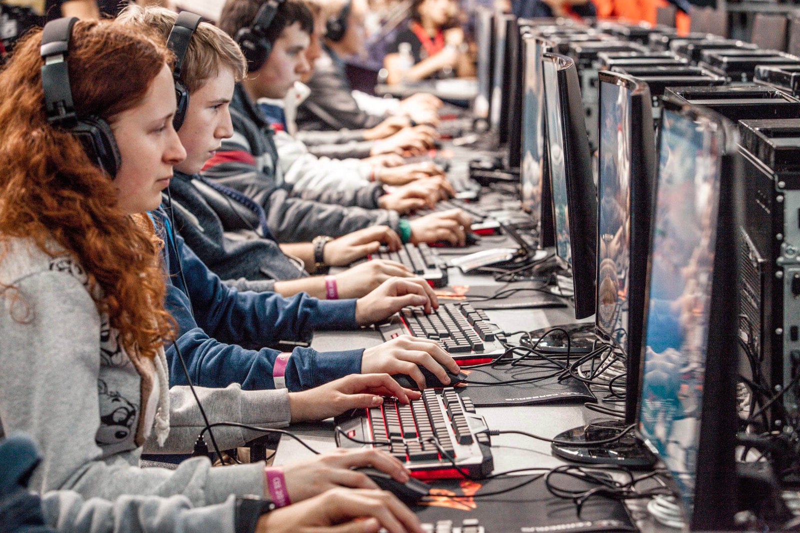 Row of gamers wearing headsets at computers, concentrating on screens in a LAN party setting.